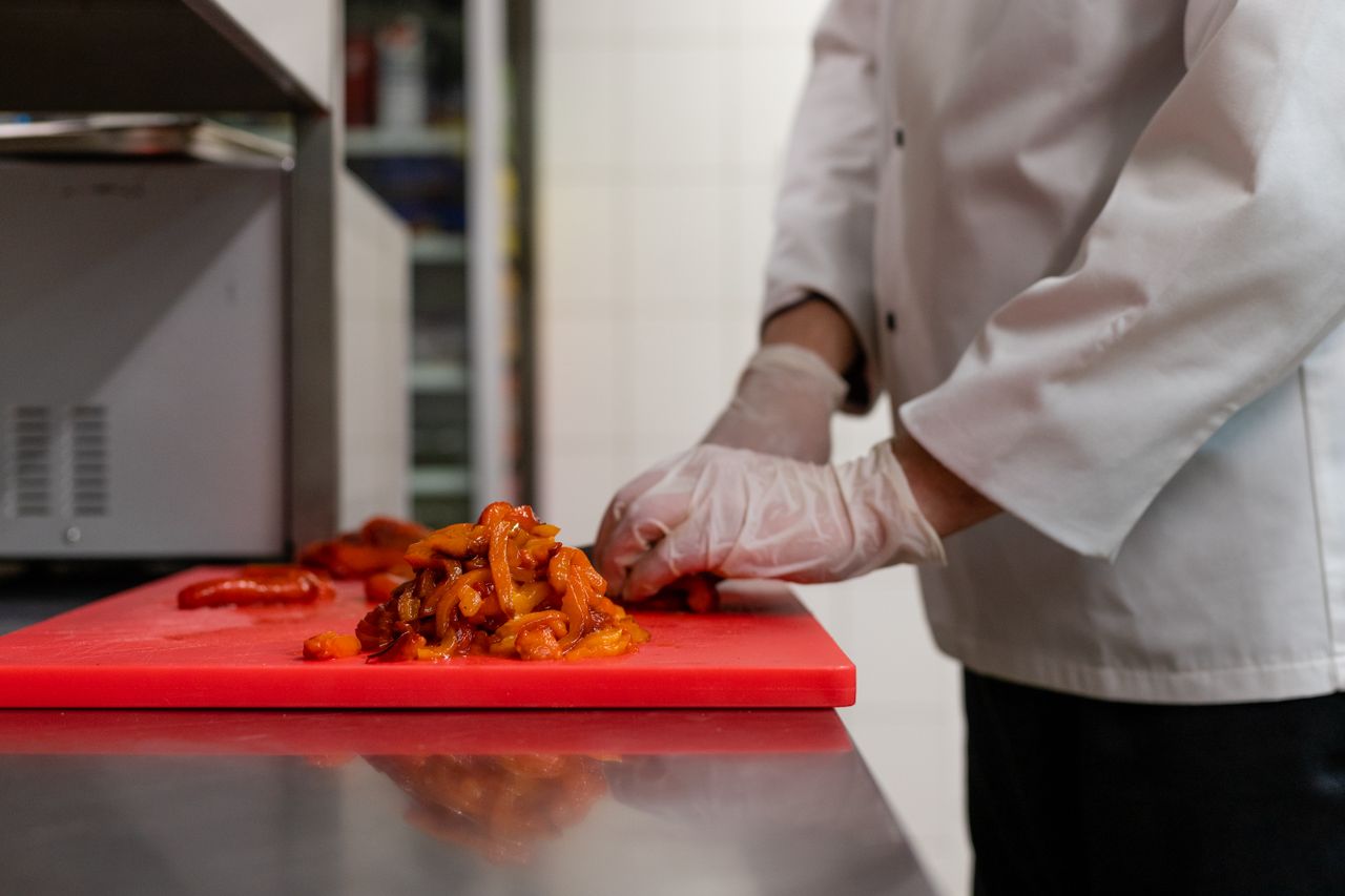 why-choose-us Chef chopping vegetables on a red cutting board in a professional kitchen.