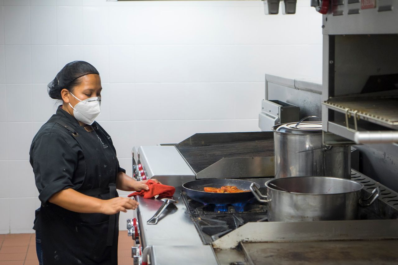 services-bg Chef busy at work in a commercial kitchen, preparing dishes while wearing a protective mask.